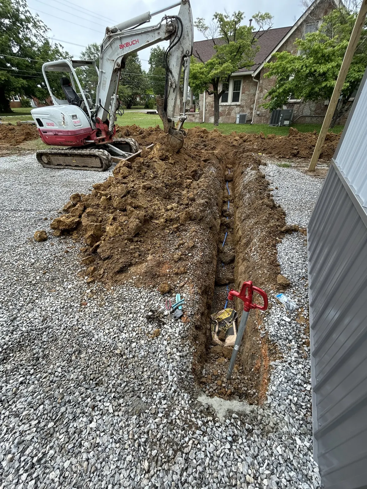 A mini excavator beside a dug utility trench