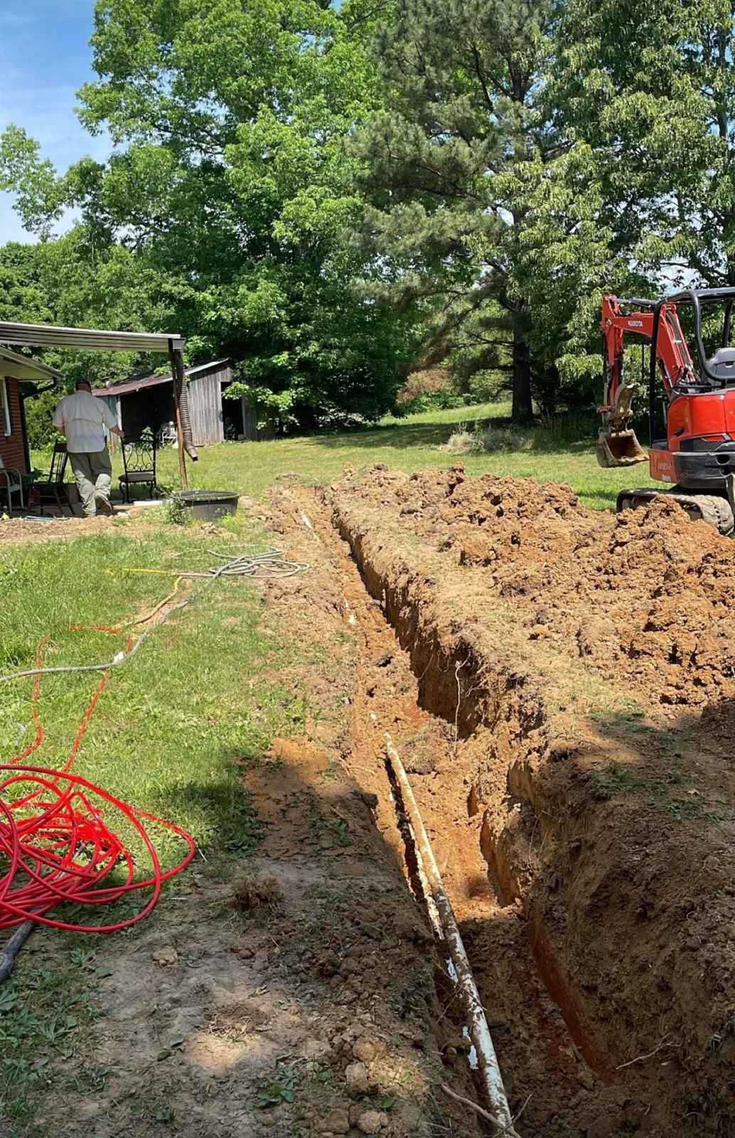 A mini excavator beside an open trench with a water line laid in it